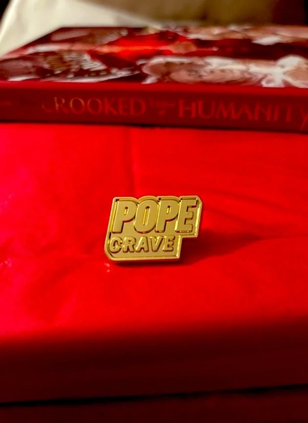 PopeCrave Pin lying on a wrapped red Conclave Zine